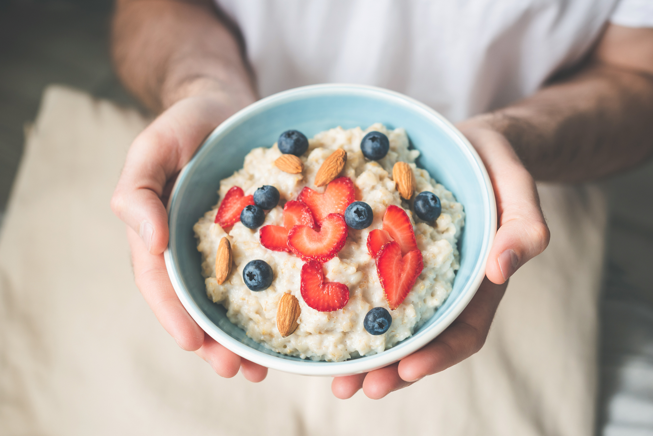 Breakfast oatmeal porridge bowl with berries and nuts in hands